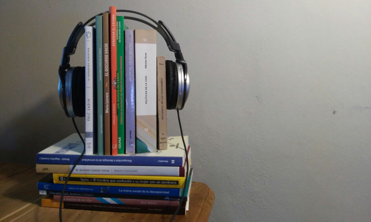 La imagen muestra un grupo de libros con unos auriculares puestos, aludiendo a los audiolibros accesibles.