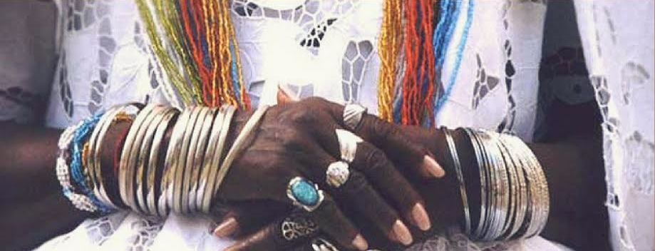 La imagen muestra ambas manos de una persona africana apoyadas una sobre otra, con anillos y pulseras.