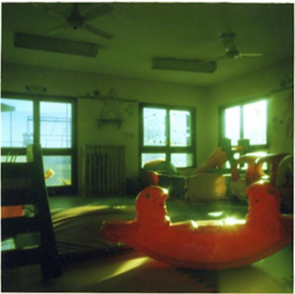 Se muestra una fotografía estenopeica en tonos verdes de una sala con juegos y juguetes para niños.